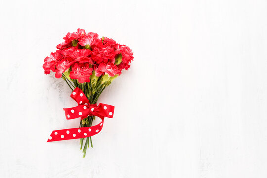 Red carnations flowers bouquet decorated with red ribbon on a white wooden background