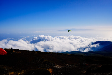 Paragliding above mountain peaks and white clouds during winter blue sunny day.
