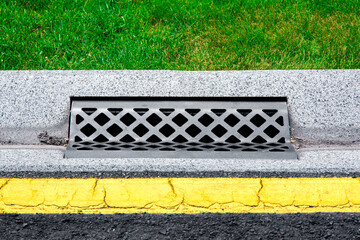 gray gutter of a stormwater drainage system on the side of asphalt road with yellow markings and...