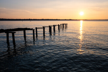 An old ramshackle pier with broken boards, during a beautiful sunset on a quiet lake.