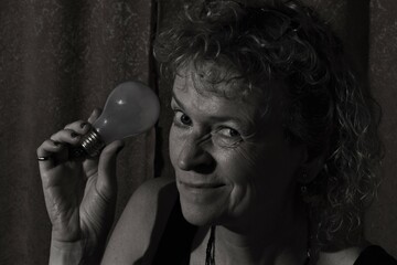 Middle aged caucasian woman, frowning with light bulb. Black and white.