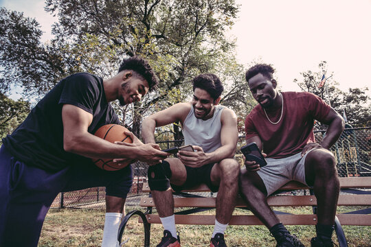 USA, Pennsylvania, Philadelphia, Male friends looking at smart phones at basketball court