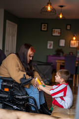 Woman on wheelchair putting on soccer shoe on sons foot in living room