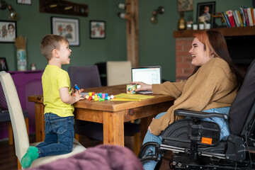 Woman on wheelchair sitting at table with son - obrazy, fototapety, plakaty