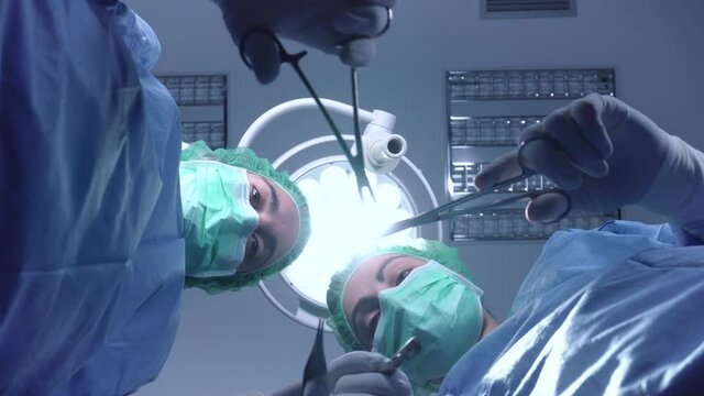 From below female surgeons in medical uniform using professional tools while standing under bright light in operating theater. High quality 4k footage