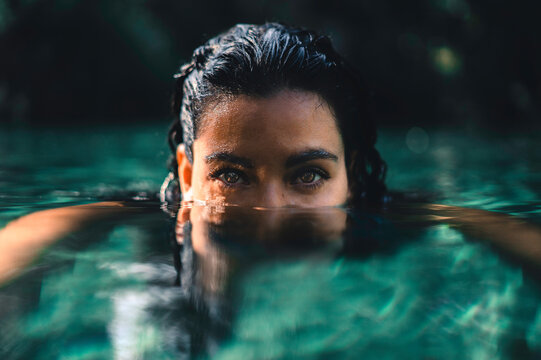 Retrato close up de una mujer joven con cabello chino y ojos caf&eacute;s hermosos nadando en el mar, con media cara sumergida bajo el agua