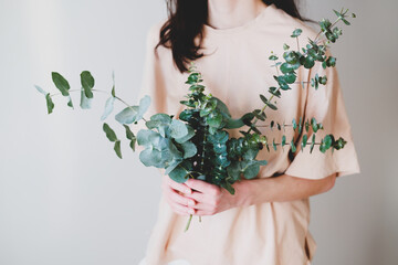 Woman holding bouquet made of eucalyptus green branches in her hands.