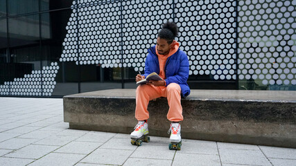 Young man in roller skates reading book outdoors