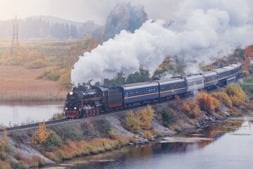 Fototapeta na wymiar Retro steam train moves along the lake at autumn morning. Karelia. Russia.