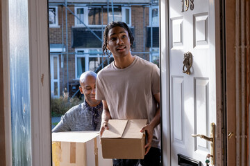 Father and son entering house with cardboard boxes