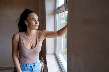 Smiling woman looking through window in house under renovation