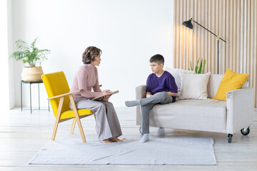 Consultation of modern teenage psychologist in cozy office. Teen boy in purple t-shirt. Children's mental health. - obrazy, fototapety, plakaty