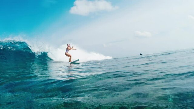 Beginner woman surfer rides the ocean wave in Maldives