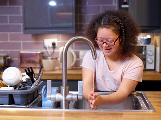 Girl with Down Syndrome washing hands in kitchen sink