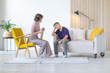 Teenager holds his head and worries. Woman psychologist listens to him with emotion. Appointment with teenage psychologist. School psychologist.