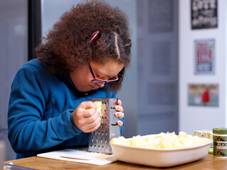 Girl with Down Syndrome grating cheese in kitchen