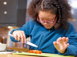 Girl with Down Syndrome cutting cherry tomato in kitchen