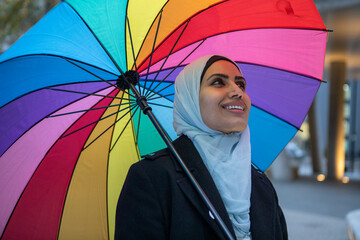 UK, London, Smiling woman in hijab holding colorful umbrella © Cultura Creative