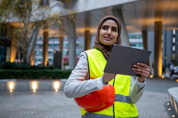 UK, London, Female engineer in hijab and reflective clothing using tablet - obrazy, fototapety, plakaty