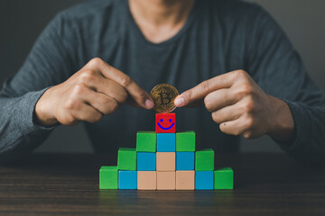 Satisfaction survey concept. The hand of a businessman holding a bitcoin and chooses a very smile face on a red woodblock cube.