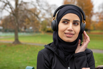 Smiling woman in hijab listening to music in park