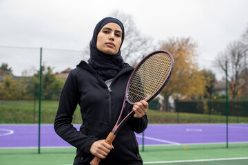 Portrait of woman in black sports clothing and hijab holding tennis racket