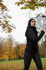 Woman in black sports clothing and hijab walking in park
