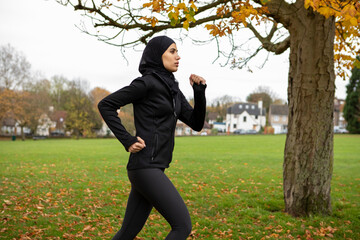 Woman in black sports clothing and hijab jogging in park