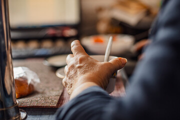 Elderly Hands of old woman with age spots and wrinkles holding cup of hot coffee during tea party....