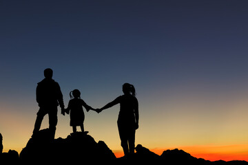Silhouette family holding hands enjoying sunset sky on top mountain.