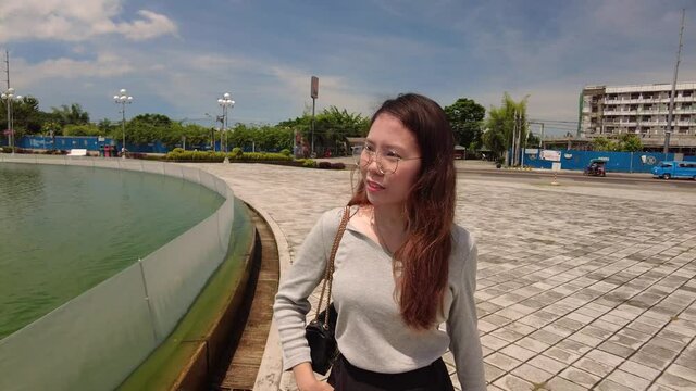 A girl walking around the New Government Center fountain area. Following her walk while facing her.