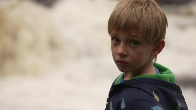 Slow motion portrait of a little boy watching the fury of white water rapids.