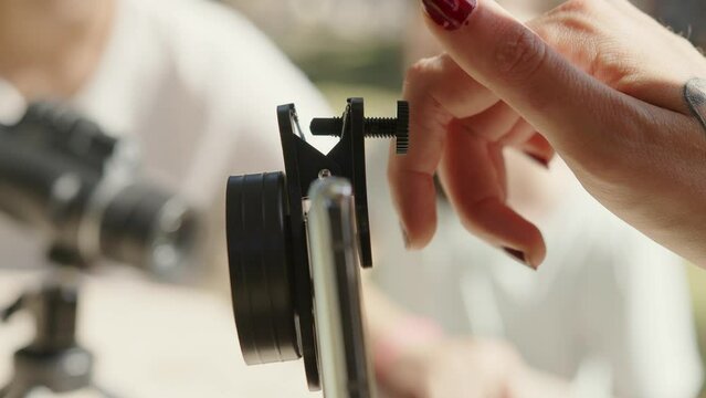 A close-up of a woman's hands adjusting a monocular telescope accessory on a smartphone.