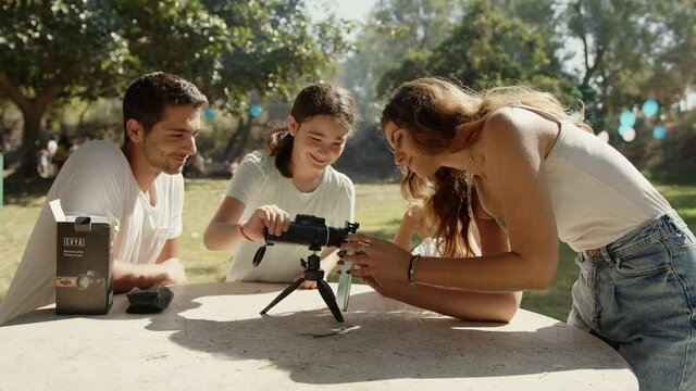 Mom puts a monocular telescope accessory on a smartphone while her family watches.