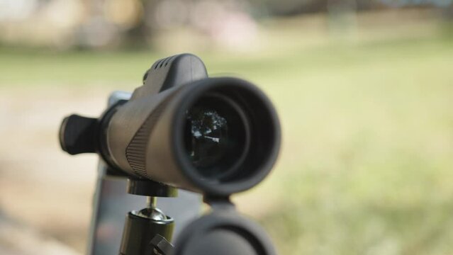 A close-up of a monocular telescope at the park on a stone surface on a sunny day.