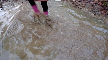 Spring puddle.Girl in pink rubber boots walks through the puddles.Spring mud and puddles.Spring weather and nature. 
