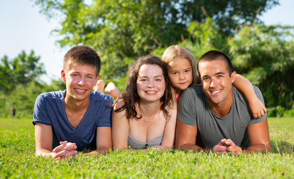 Portrait of positive family on green lawn in summer park. High quality photo