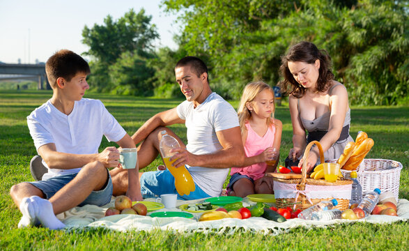 Happy parents with two kids having picnic together on green meadow in park. High quality photo