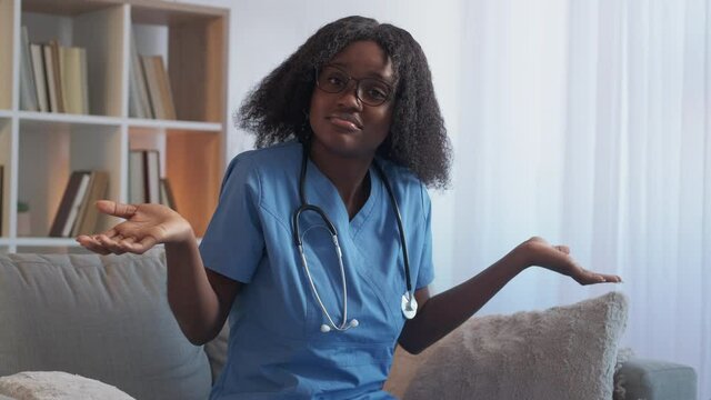 Confused doctor. Medical question. Medicine doubt. Unsure woman nurse shrugging shoulders uncertain with diagnosis treatment on couch at hospital.