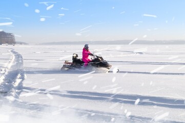 Fototapeta na wymiar A girl rides a snowmobile through a snow-covered field. Riding on winter modes of transport. Active recreation. Snowmobiling in winter. Selective focus