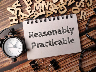 Clock,glasses,paper clips and notebook with text Reasonably Practicable on a wooden background.