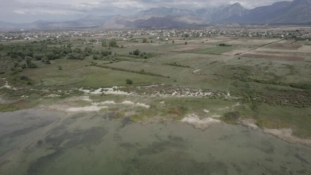 Video with a drone over the Skadar Lake in Albania, from a descriptive plane with reverse leaving the Grude Fushe village on the horizon with the mountains.