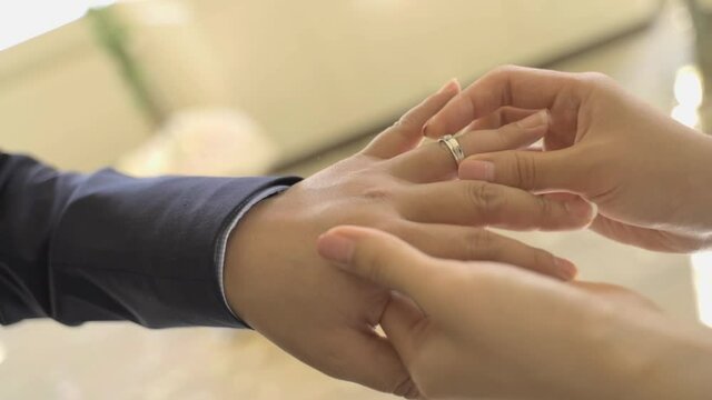 A woman's hand slowly puts a wedding ring on a man's hand