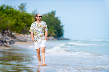 Portrait of Caucasian man in beach clothes and sunglasses walking on tropical beach in summer sunny...