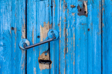 An old wooden door, with cracked blue paint and holes.
