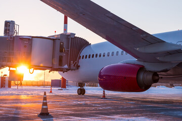 Close-up passenger jet plane near the boarding gate on the background of sunset in winter