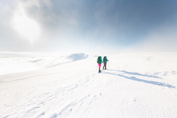 Two women walk in snowshoes in the mountains