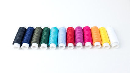Multi-colored threads for sewing lie in two rows on a background of white cotton fabric.
sewing threads.
