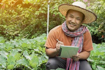 Asian middle-aged farmer wears loincloth, is using taplet to record his plant growing data in the backyard of this house in lately morning.