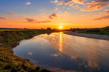 Obraz premium Amazing view at scenic landscape on a beautiful river and colorful sunset with reflection on water surface and glow on a background, spring season landscape